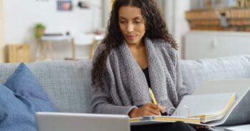 Woman sitting on couch with laptop and binder, working.
