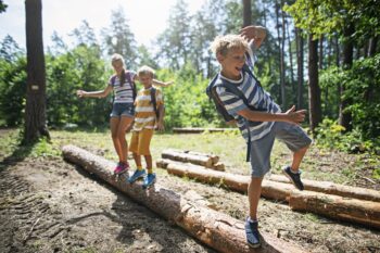 Happy kids hiking in a forest. Children are walking on a tree trunks, balancing with arms outstretched. Boys are aged 10 the girl is 13.