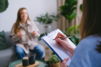 Behavioral health provider taking notes on a clipboard while a youth client speaks during a psychoeducation session